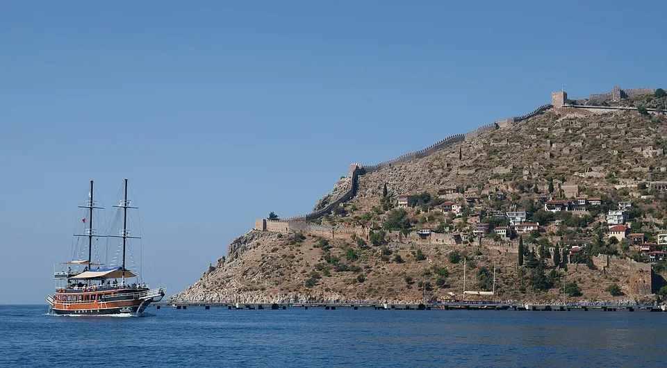 Ausflugsboot vor der Felshalbinsel von Alanya mit Burgmauern und türkisfarbenem Wasser