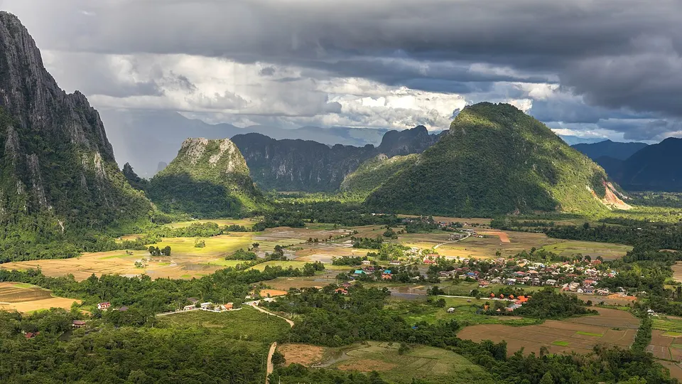 Laos: Karst peaks and green paddy fields under a stormy sky, South view from the top of Mount Nam Xay, during the monsoon, in Vang Vieng, Vientian