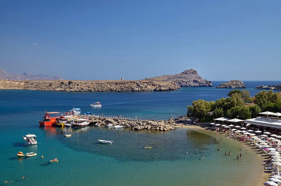 Holzsteg in der Bucht von Lindos auf Rhodos mit klarem Wasser und weißem Dorf am Hang